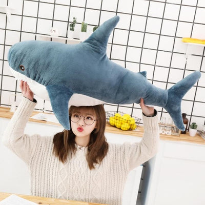 Woman holding a kawaii shark plushie in the kitchen above her head