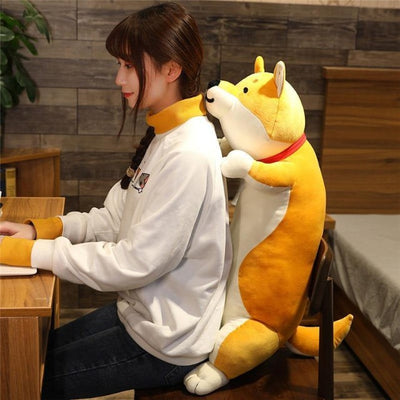 A smiling dog plush toy behind a woman on a laptop