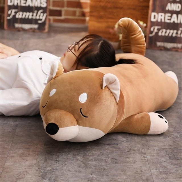 A girl laying her head on a big shiba inu plush pillow that is sleeping